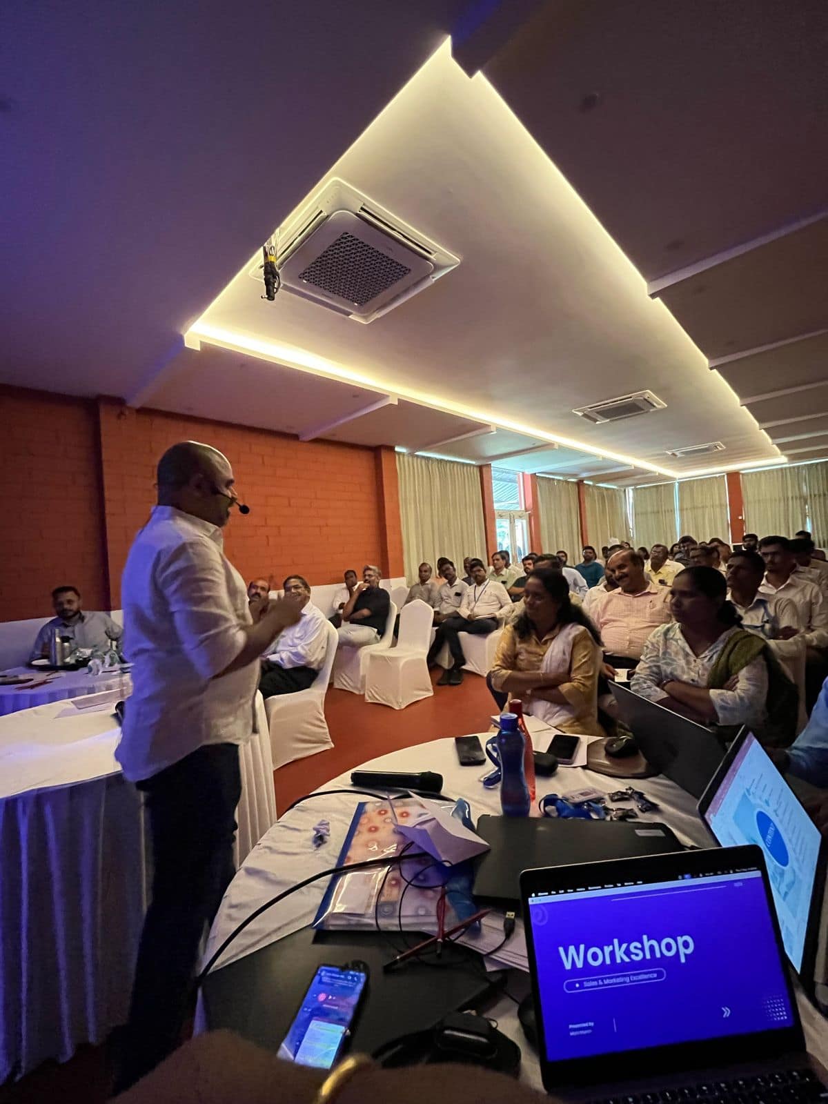 Maran presenting to a full room at a sales and marketing workshop, a laptop on the front table showing the opening slide