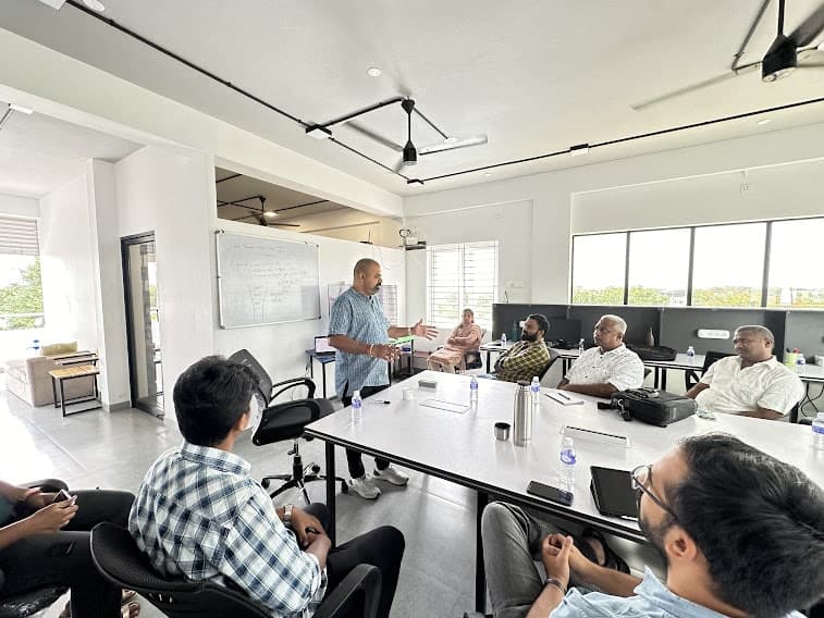 A workshop in progress — Maran presenting at a whiteboard to a seated group around a table