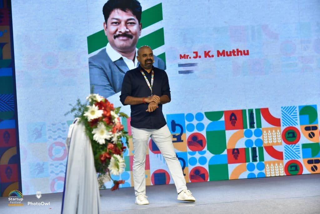 Maran on stage at the Startup Festival, a speaker board and festival artwork on the screen behind him
