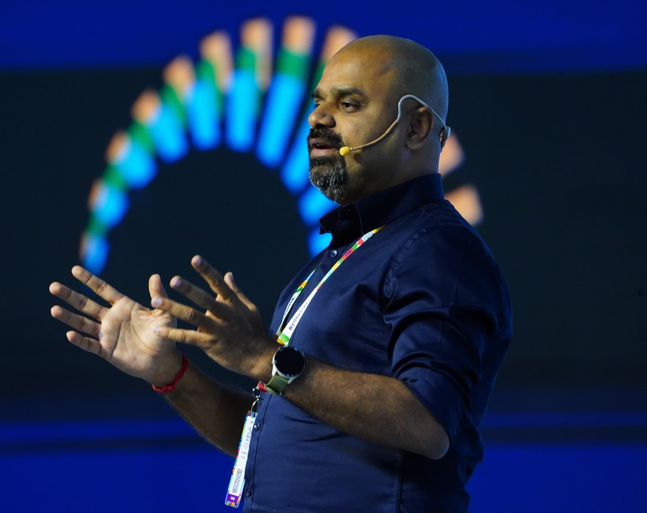 Maran speaking on stage with a headset microphone, hands mid-gesture